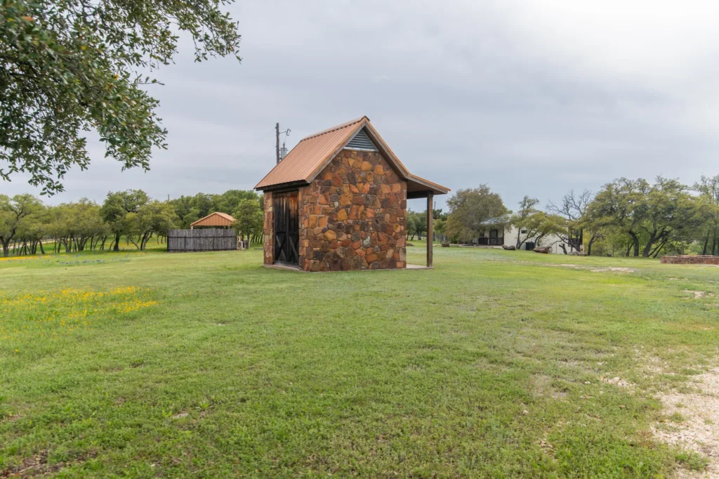 A rustic stone cabin surrounded by a lush green field and trees under a cloudy sky, illustrating a peaceful healing retreat setting.