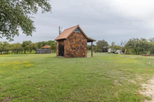 A rustic stone cabin surrounded by a lush green field and trees under a cloudy sky, illustrating a peaceful healing retreat setting.